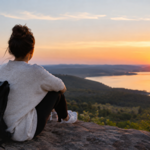 Woman sitting on a scenic overlook at sunset, reflecting on a new chapter in life.