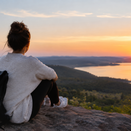 Woman sitting on a scenic overlook at sunset, reflecting on a new chapter in life.